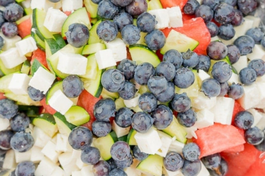Watermelon feta salad ingredients mixed together including blueberries, watermelon chunks, cucumber slices, and feta cheese