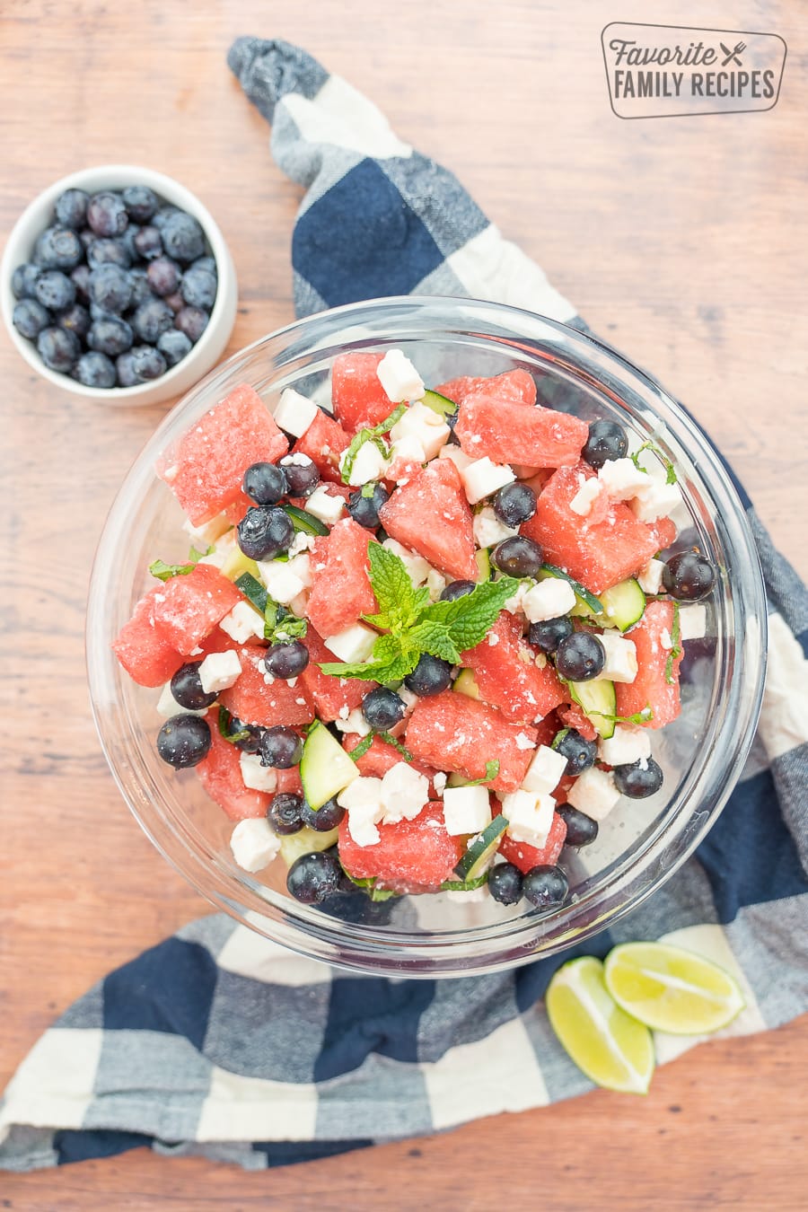 Watermelon feta salad in a glass bowl with a bowl of blueberries and limes