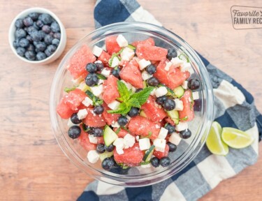 Watermelon feta salad in a glass bowl with limes and a bowl of blueberries