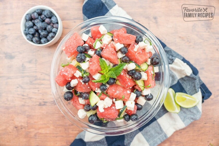 Watermelon feta salad in a glass bowl with limes and a bowl of blueberries