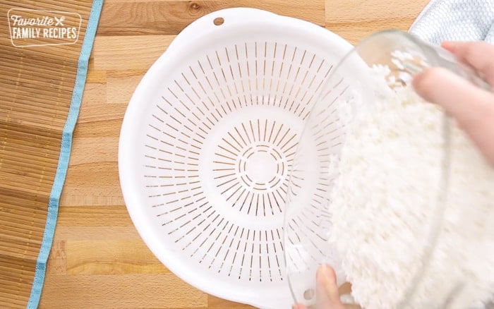 Rice being rinsed and poured into a colander to make sushi rice