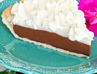 A slice of chocolate haupia pie on a turquoise plate with flowers in the background