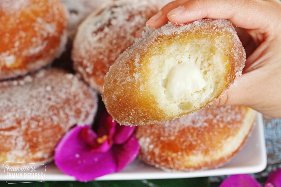 malasada with a bite out of it showing the soft center and haupia filling
