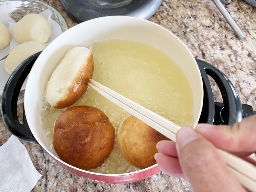 malasadas being fried and turned over with chopsticks