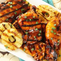 A platter of huli huli chicken with grilled pineapple slices on the side