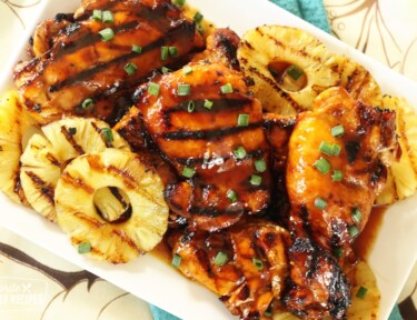 A platter of huli huli chicken with grilled pineapple slices on the side