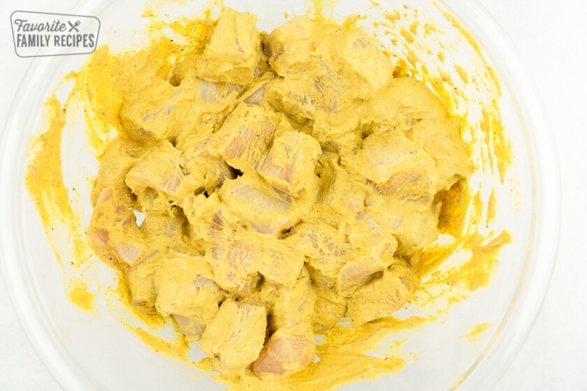 Raw diced chicken with Tikka Masala sauce in a clear bowl.
