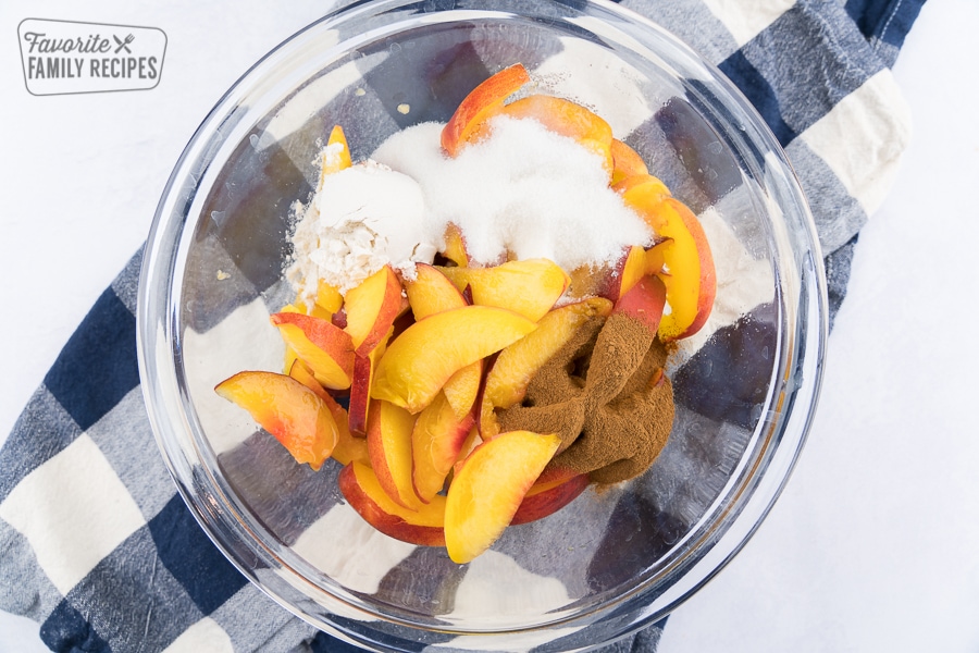 A glass bowl with peaches and ingredients being mixed together.