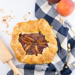 Peach galette with blue checkered towel with peaches on the side.