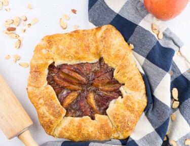 Peach galette with blue checkered towel with peaches on the side.