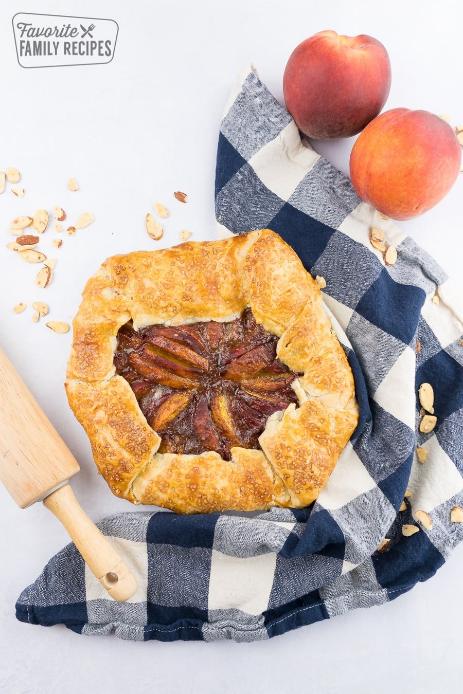 Peach galette with blue checkered towel with peaches on the side.