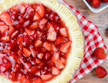 Strawberry pie with a red checkered table cloth behind the glass plate.