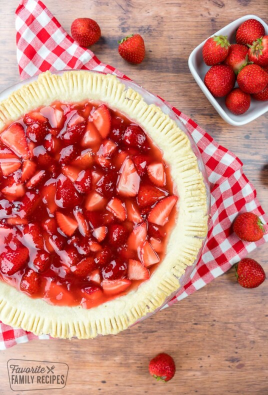 Strawberry pie with a red checkered table cloth behind the glass plate.