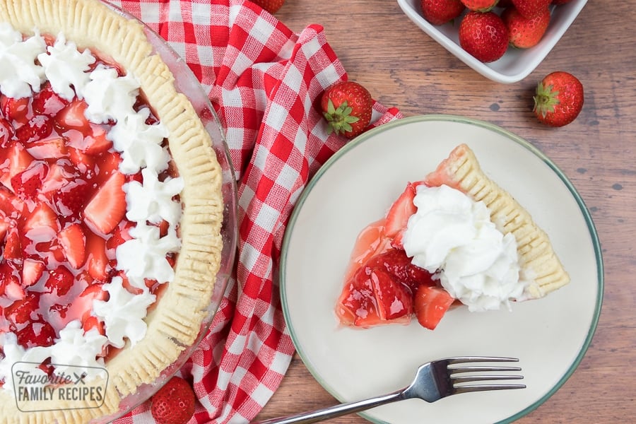 a slice of fresh strawberry pie on a plate topped with whipped cream.