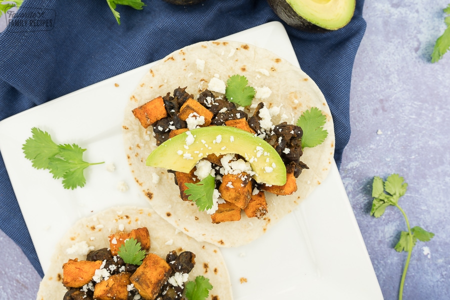 A taco with sweet potatoes, black beans, avocado, cilantro, and cotija cheese