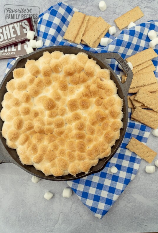 S'mores dip in a cast iron skillet surrounded by graham crackers, mini marshmallows, and hershey's bars