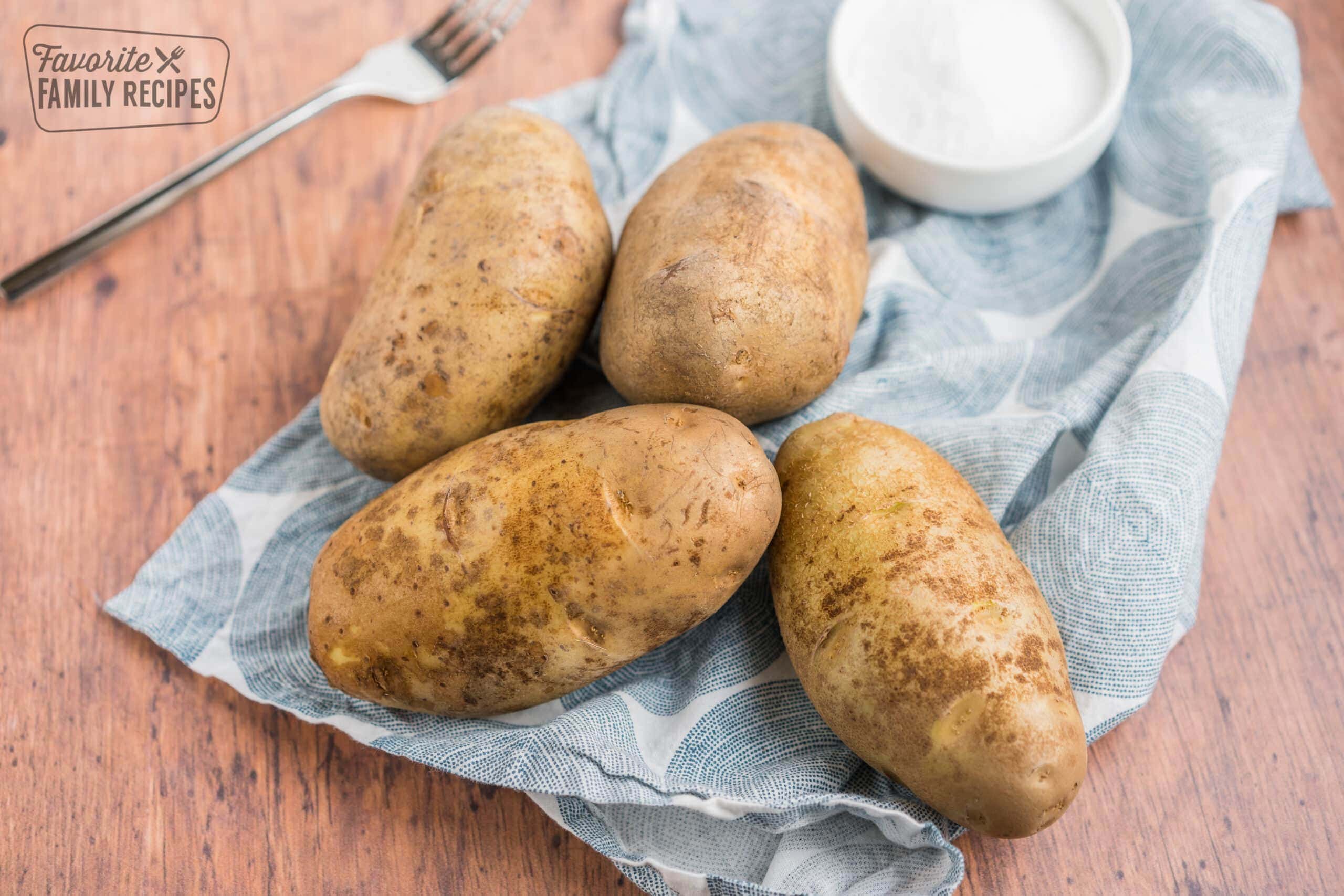 four raw potatoes on a dishcloth with a fork and a bowl of salt