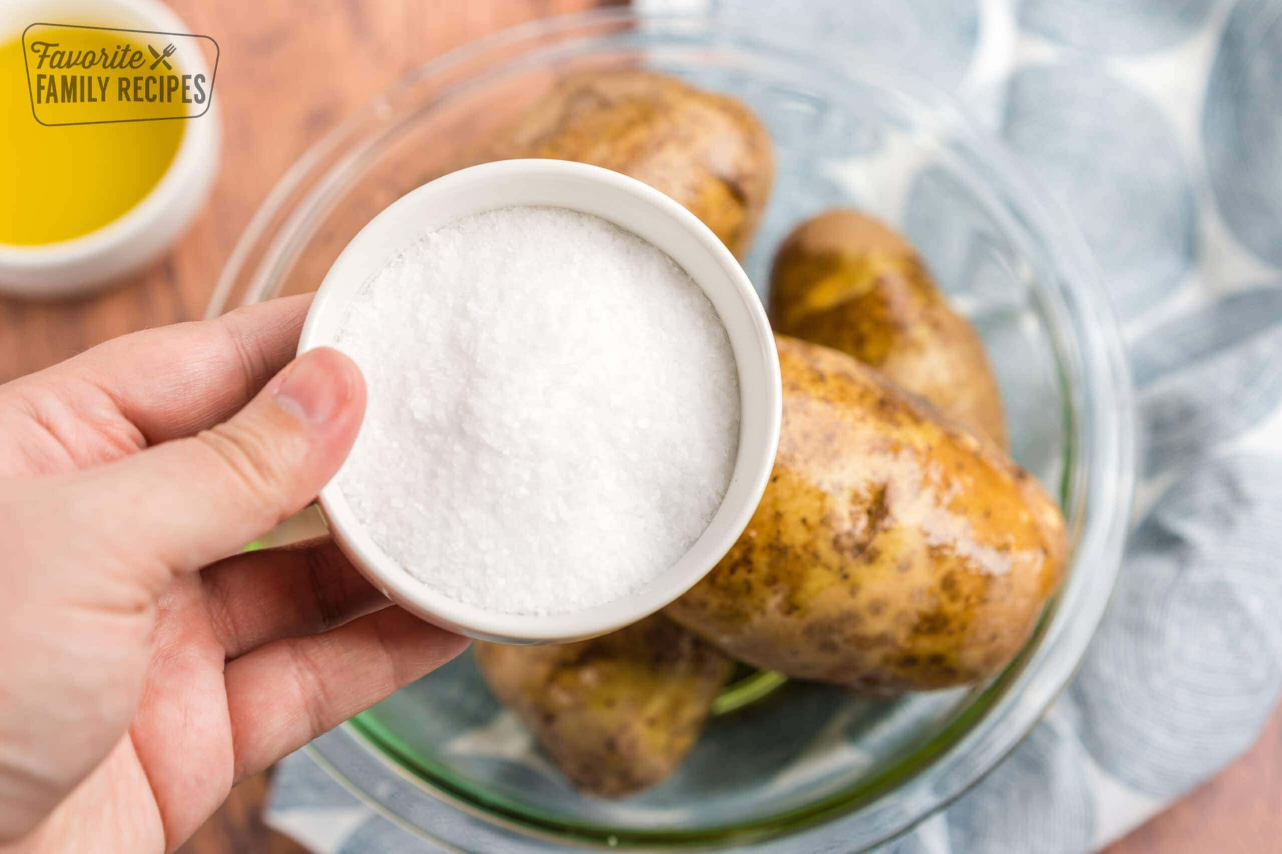 A bowl of salt going on top of potatoes