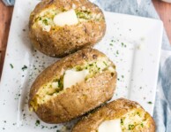 Three baked potatoes with butter and herbs and a bowl of herbs