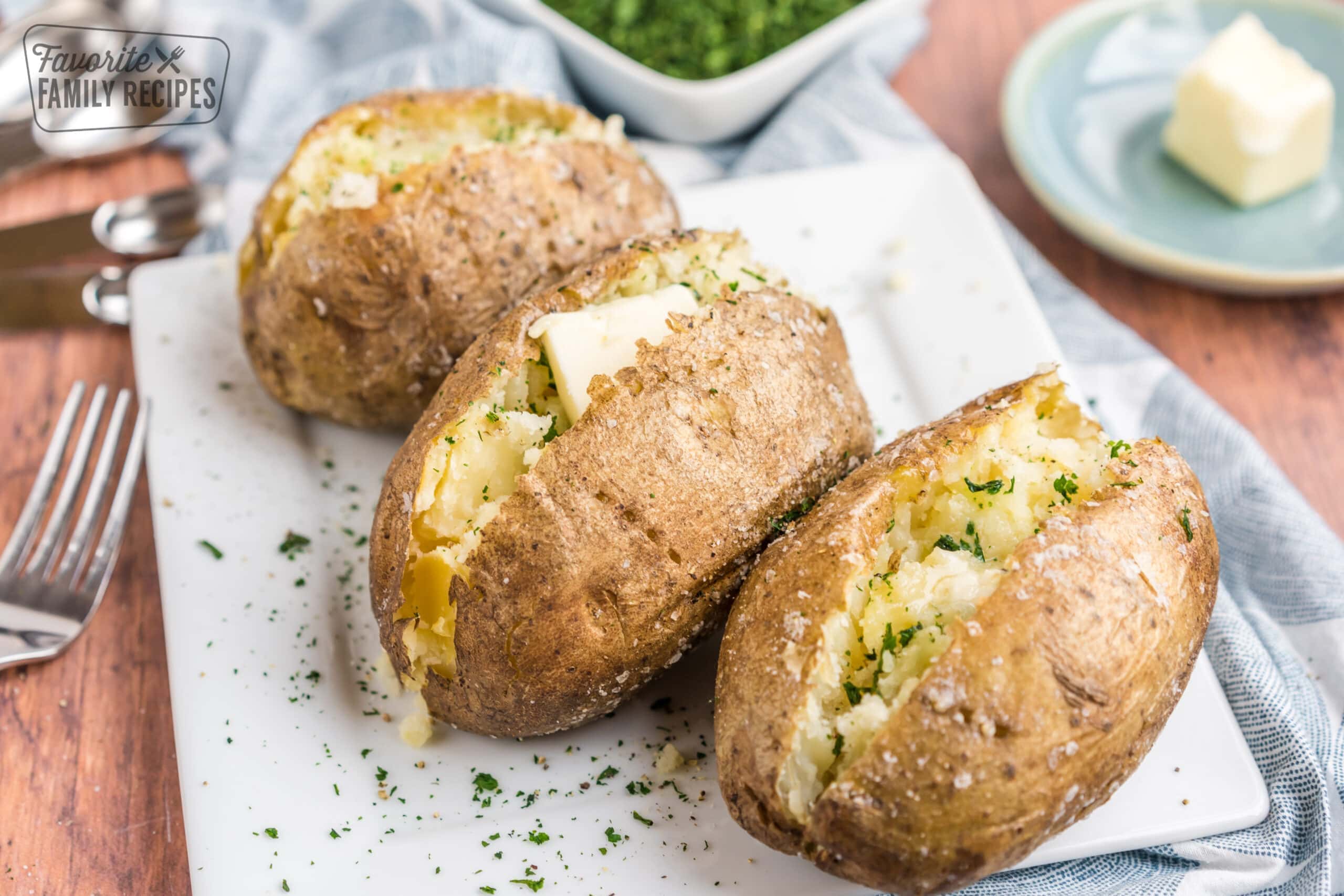 Three baked potatoes on a plate with butter and herbs.