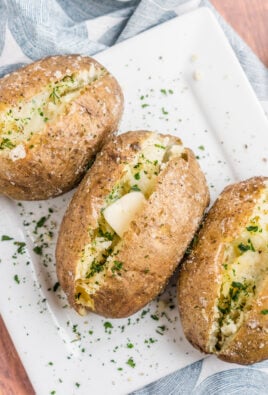 Three baked potatoes on a plate topped with butter and herbs