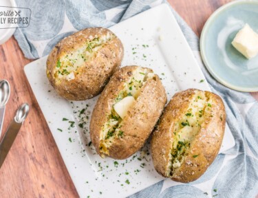 Three baked potatoes on a plate topped with butter and herbs