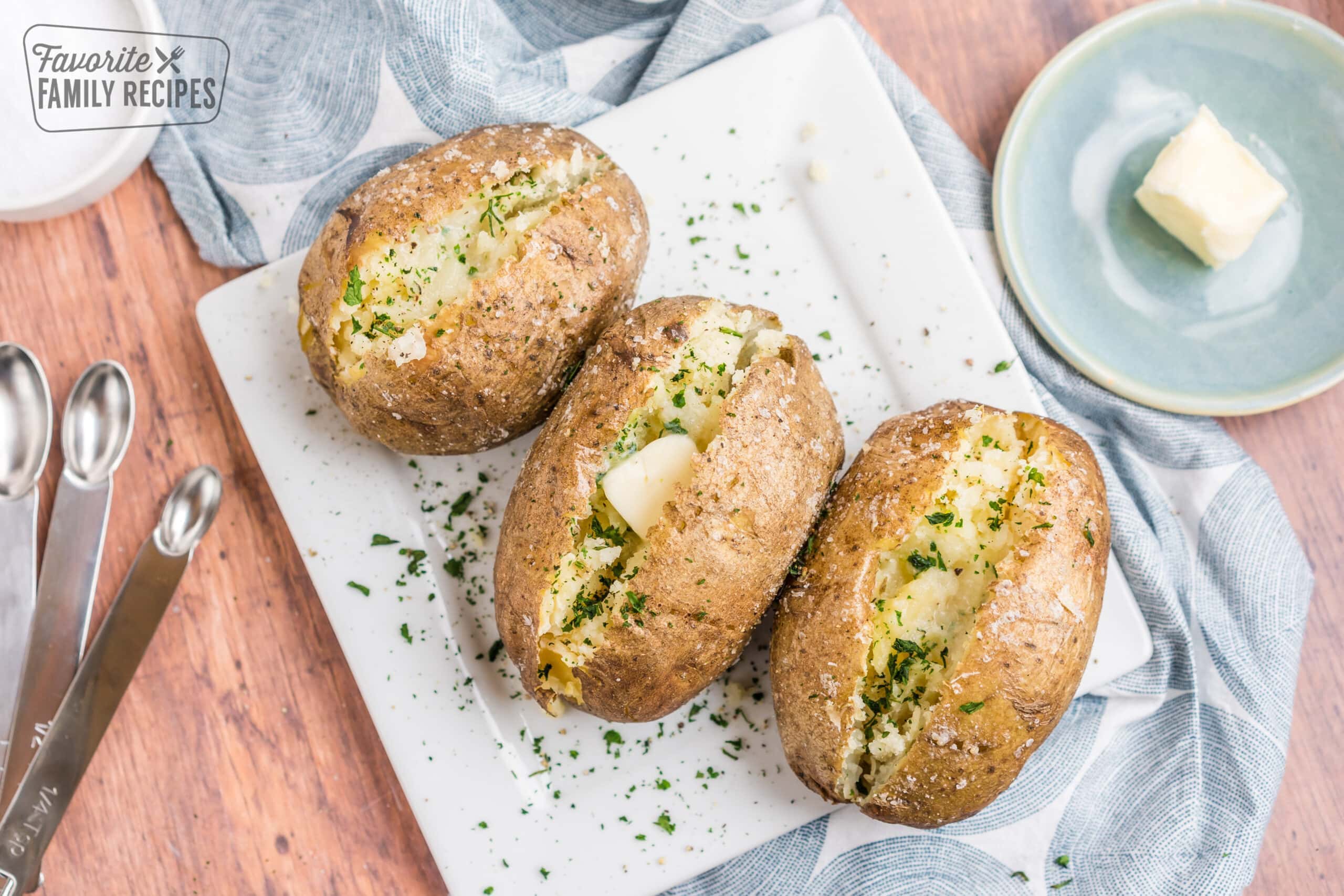 Three baked potatoes on a plate topped with butter and herbs.