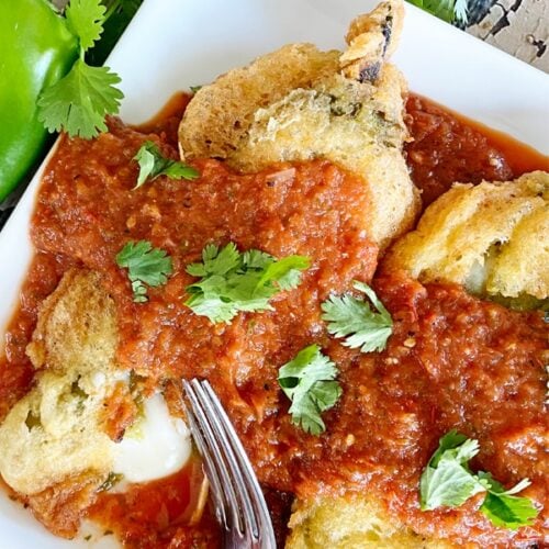 Vertical image of chiles rellenos on a plate with sauce