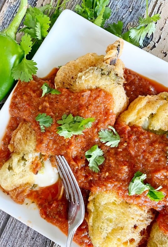 Vertical image of chiles rellenos on a plate with sauce