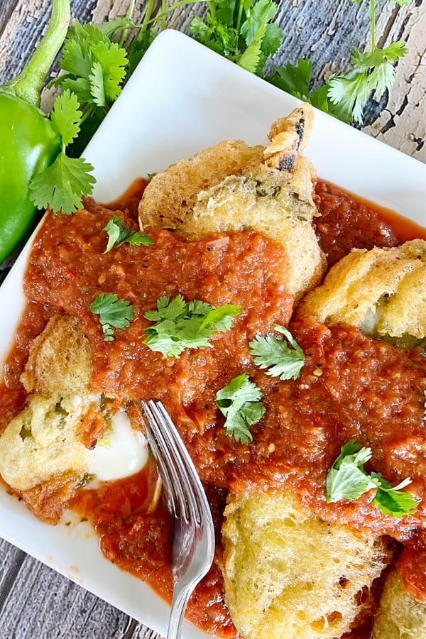 Vertical image of chiles rellenos on a plate with sauce