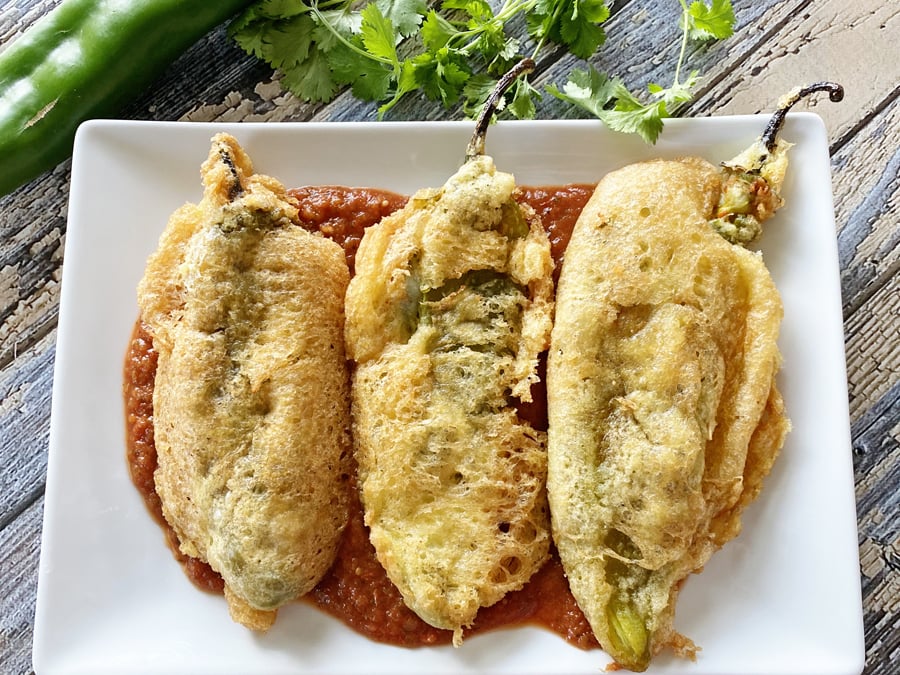 Chile rellenos on a plate with sauce.