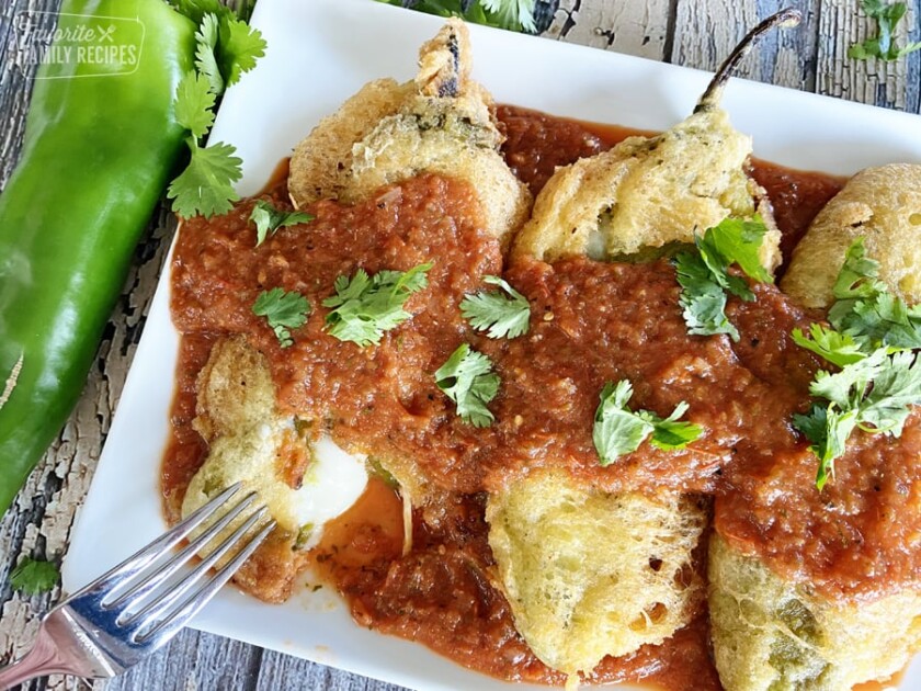 Chiles rellenos with red sauce being cut with a fork showing cheese