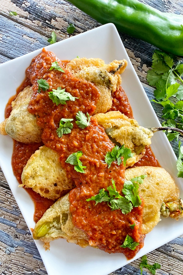 Chiles rellenos on a plate with red sauce over the top