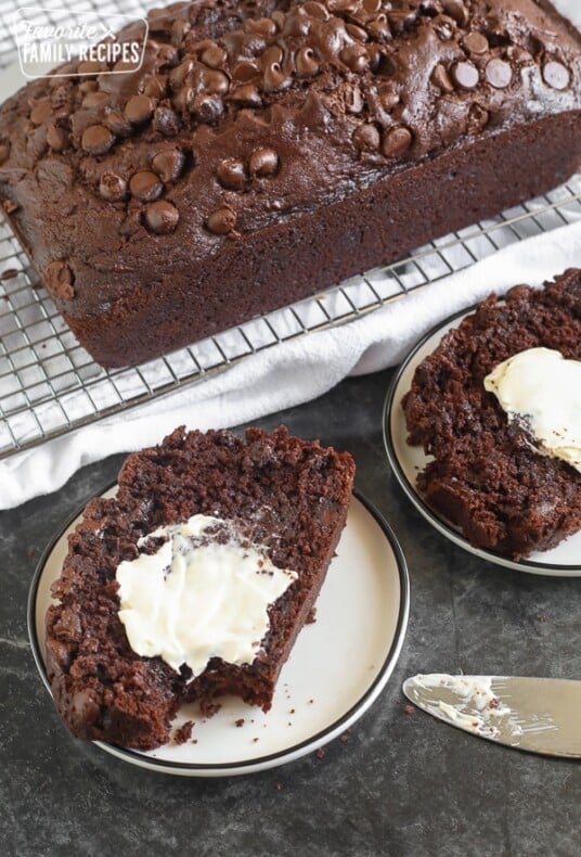 A slice of chocolate zucchini bread on a plate with butter spread on top.