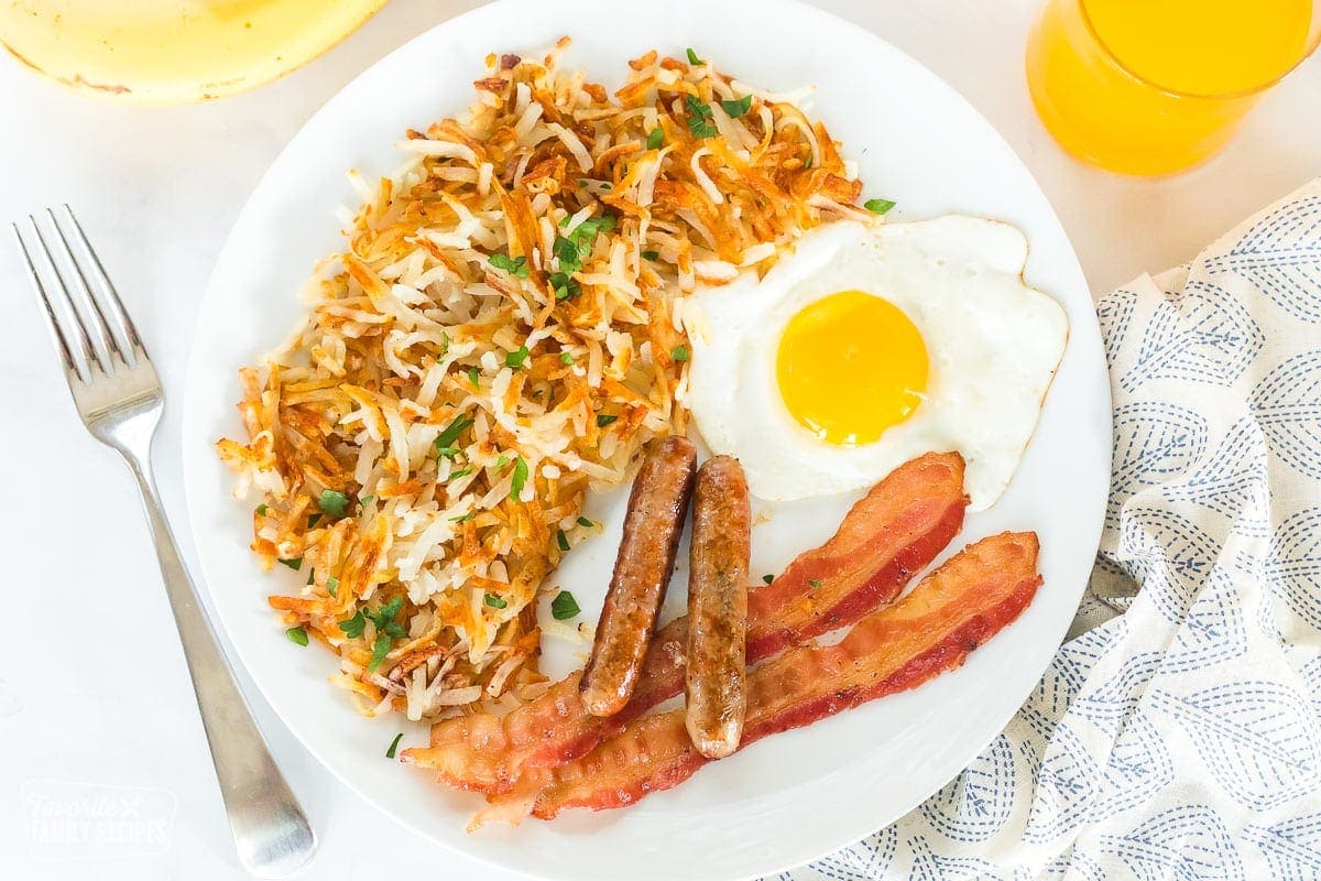 A breakfast plate with hash browns, sausage, eggs, and bacon.