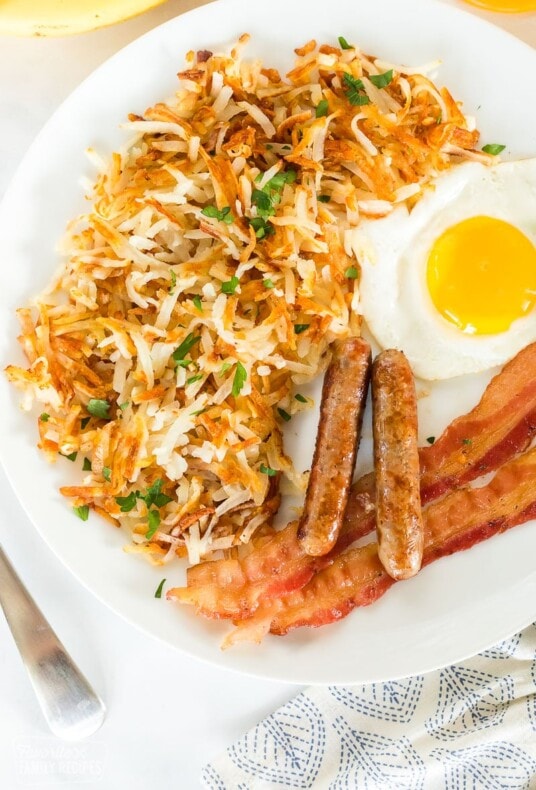 Cooked hash browns on a breakfast plate with bacon, eggs, and sausage