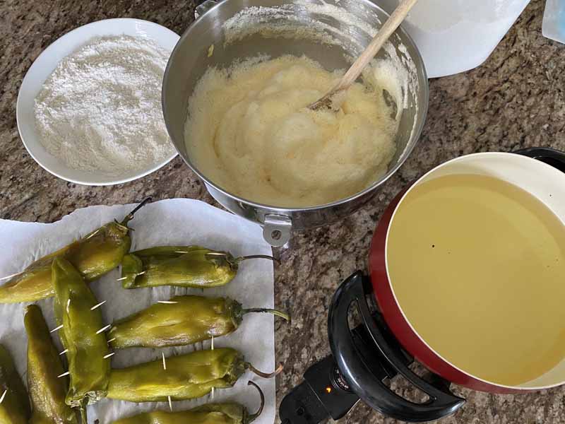 chiles rellenos assembly line with flour, batter, and hot oil