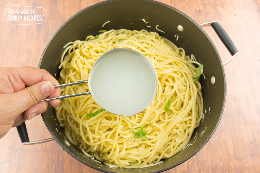 A measuring cup full of pasta water over a pot of pasta.