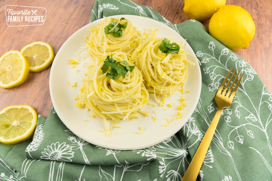 lemon spaghetti twirled into nests on a plate topped with basil, lemon zest, and parmesan cheese.