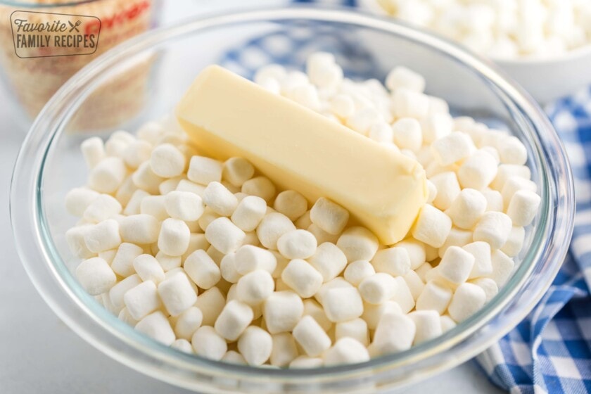 A glass bowl filled with mini marshmallows and a stick of butter on top.