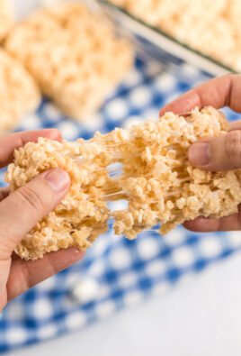 Two hands pulling apart a rice krispie treat with gooey marshmallow stretching in between the two pieces.