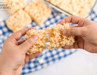 Two hands pulling apart a rice krispie treat with gooey marshmallow stretching in between the two pieces