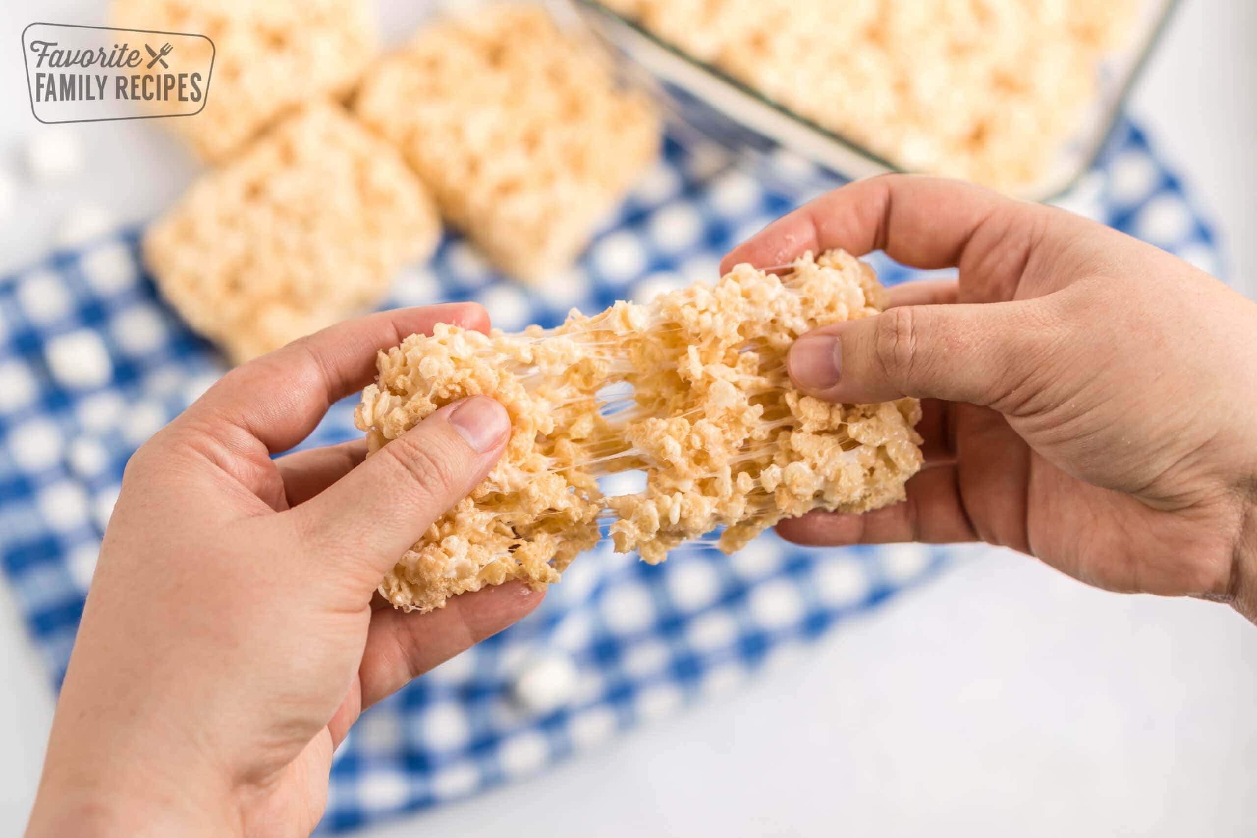 Two hands pulling apart a rice krispie treat with gooey marshmallow stretching in between the two pieces