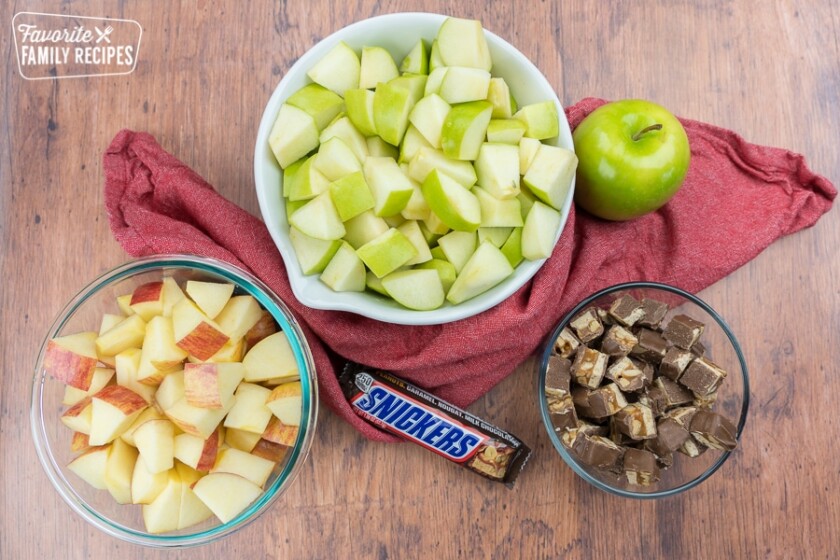 A bowl of chopped granny smith apples, a bowl of chopped gala apples, and a bowl of chopped snickers