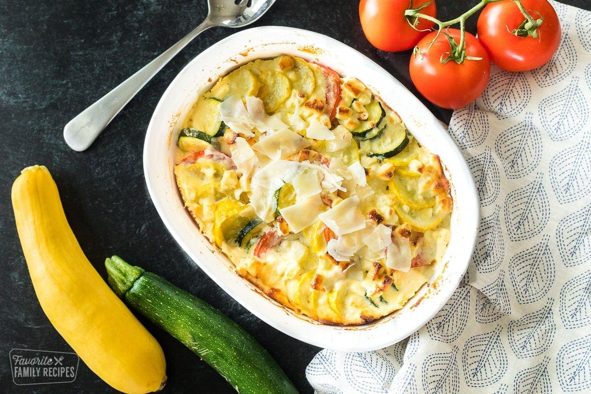 Yellow squash, zucchini, and tomatoes layered in a white casserole dish.