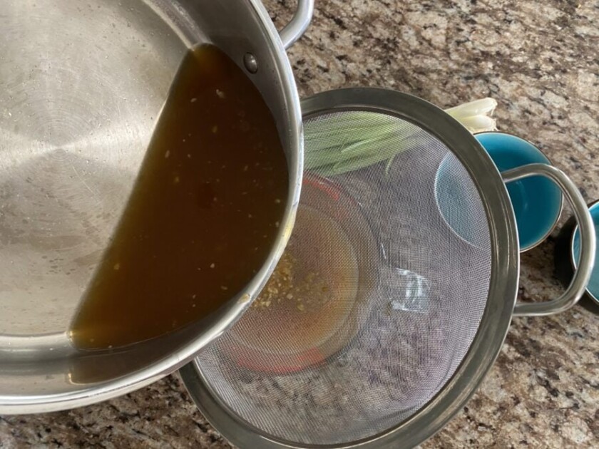 broth being strained into a measuring cup