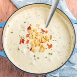 Clam chowder in a pot topped with oyster crackers and bacon