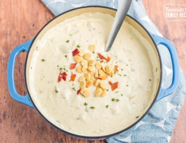 Clam chowder in a pot topped with oyster crackers and bacon