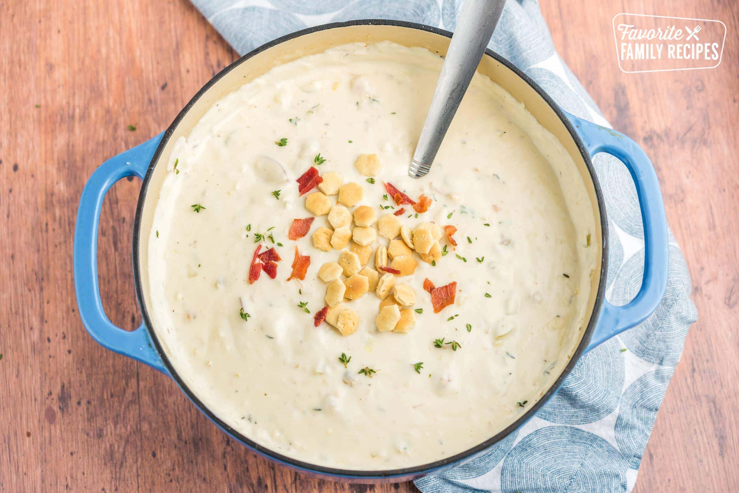 Clam chowder in a pot topped with oyster crackers and bacon