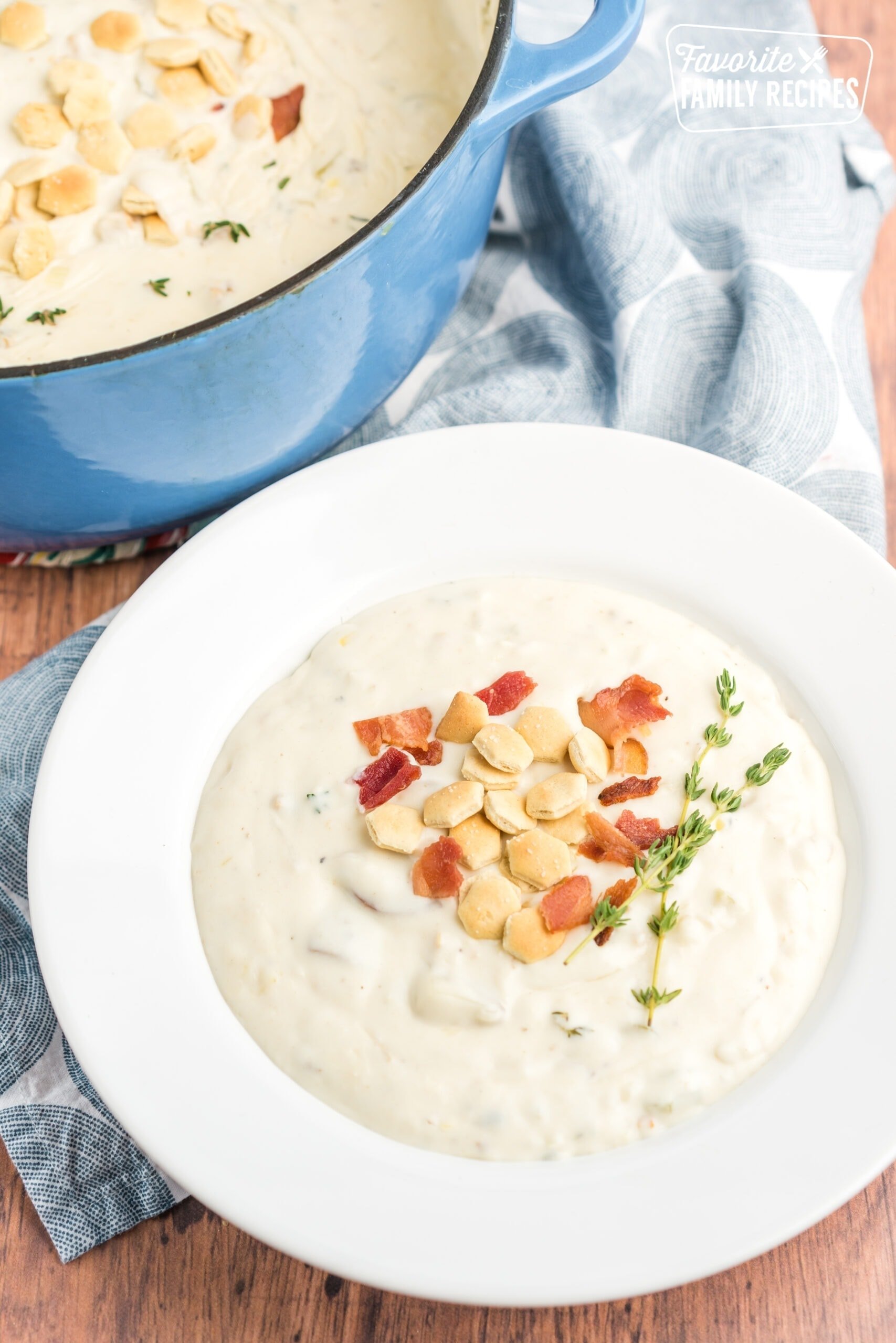 Clam chowder in a bowl topped with bacon, oyster crackers, and fresh thyme